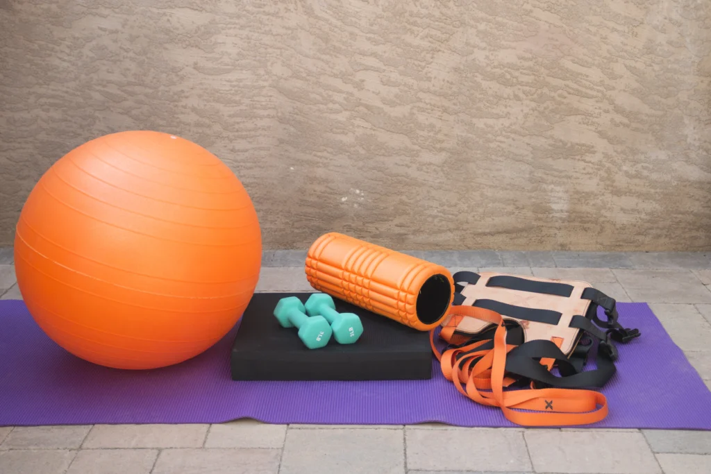 Physical therapy equipment: exercise ball, foam roller, hand weights and resistance straps on a mat